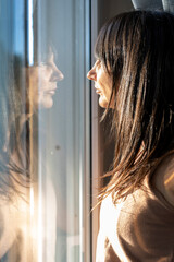 Profile portrait of thoughtful woman looking through window with reflection in sunlight © Valeria Venezia
