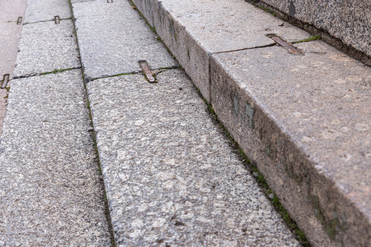 Ancient stone steps with iron anchor fittings and patches of moss and weeds, showing textured granite surfaces, wear and historic urban character ideal for architectural, heritage, and backgrounds