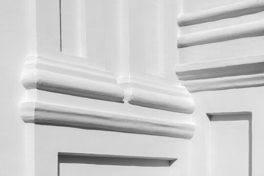 White plaster architectural molding photographed in high-contrast light showing geometric relief, clean texture and deep shadows; minimalist facade detail conveying form, pattern and classical shapes