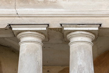 Close-up view of two weathered classical columns supporting an entablature on a historic building facade, highlighting textured stone, cracks and aged plaster that convey architectural character © evannovostro