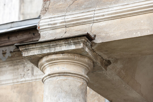 Close-up of a weathered classical stone column and entablature showing cracked plaster, aged masonry and architectural detail on a historic facade conveying decay, texture and heritage