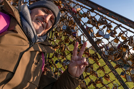 Man showing a peace sign while standing next to a fence full of love locks
