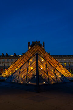Louvre pyramid glass architecture glowing under a deep blue evening sky in paris