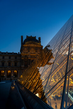 Louvre museum glass pyramid reflecting illuminated palace at dusk paris night