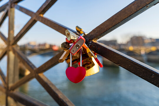 Red heart padlock hanging on pont des arts bridge in paris railing with many other love locks