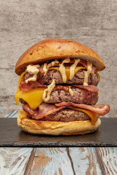 Towering triple-patty burger layered with bacon, cheddar, and mustard drizzle stacked between each beef layer