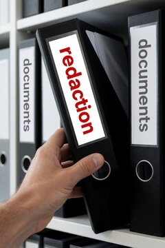 Hand pulls black binder with red redaction text from office shelf. Person organizes confidential files in archive room. Clerk handles sensitive documents, privacy data protection in legal corporate