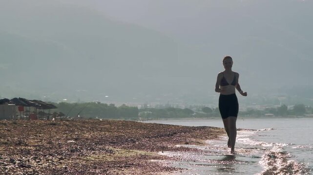A slow motion video of an eight year old female one eyed pitbull running together with her thirty year old female owner on a sunny morning sandy beach.