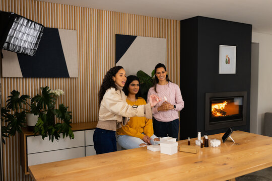 Diverse women presenting skincare products on long wooden table in studio set with tablet