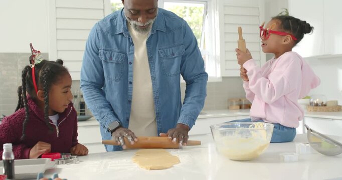 African American family man placing pin, rolling dough, child girls cutting cookies for christmas