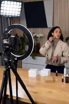African American woman showing facial tool speaking to camera in trench jacket in studio