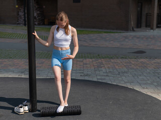 Obraz premium A Caucasian woman stretches her feet with a foam roller at a sports ground.