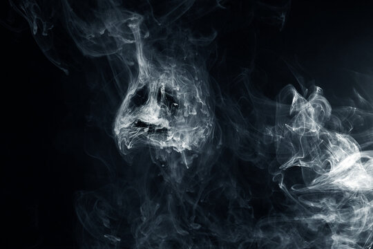Smoke forming a scary ghost skull face on dark background