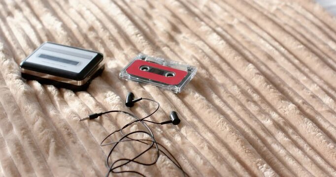 Camera is panning and reframing cassette, earbuds, metal player on ribbed blanket, tightening frame