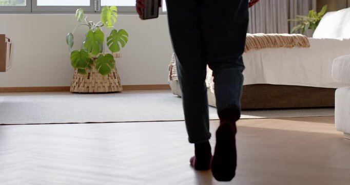 Woman in maroon top entering right, walking across floor toward window, holding book, seeking light