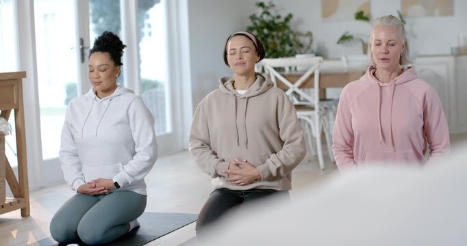 Three female friends kneeling on yoga mats following guided breathing for calm, pursing lips