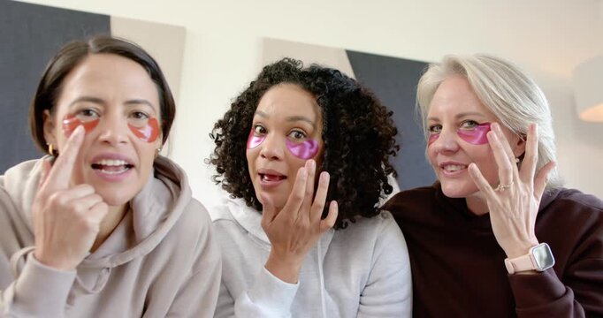 Three female friends after applying under-eye gel patches tapping, adjusting, comparing fit at home