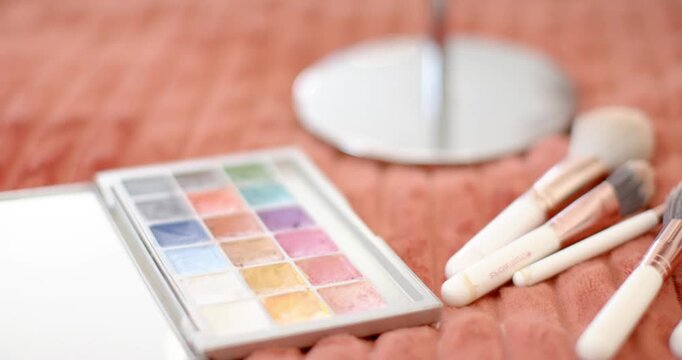 Camera is panning while hand is arranging brushes and palette for display on coral blanket