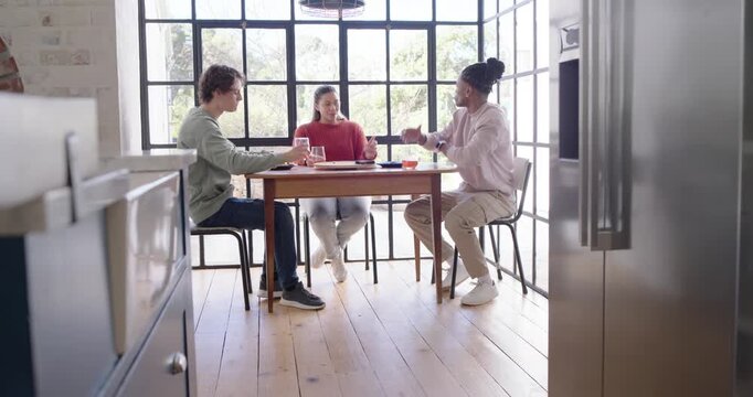Diverse friends clinking glasses, sipping orange drinks, and catching up at kitchen dining table