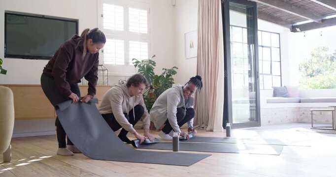 Diverse friends greeting, grabbing speaker, unrolling, aligning then rolling mats for yoga at home
