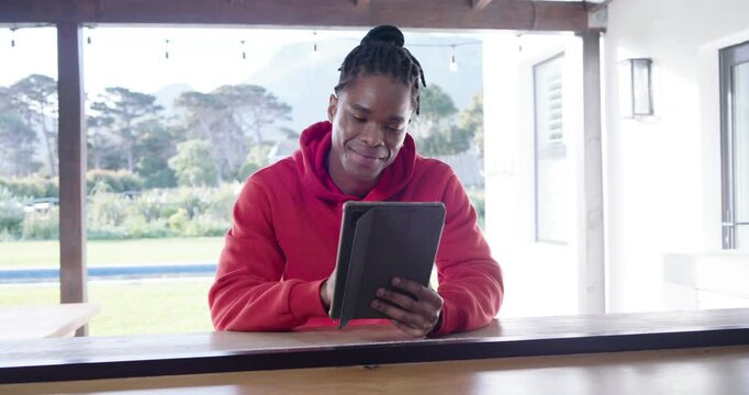 African adult male in red hoodie sitting at counter reading tablet, smiling, laughing