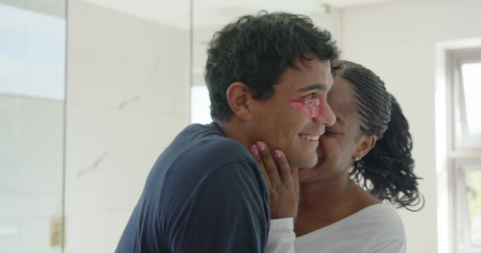 African American couple, woman placing pink under-eye patches on man to pamper in bathroom mirror
