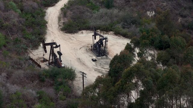 Aerial view of oil pump jacks operating in the Baldwin Hills area surrounded by trees and dirt paths in Los Angeles, California, United States.