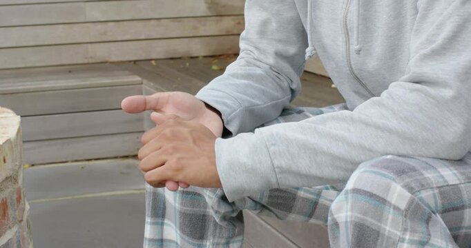 African man in hoodie and pants rubbing palms, turning to camera, smiling while relaxing on bench