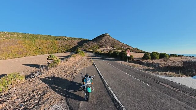 Ascending camera movement revealing a turquoise custom motorcycle parked at the edge of a country road, creating an aerial perspective over the surrounding rural landscape.