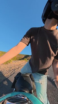 Vertical slow motion rear facing action camera view from the motorcycle handlebar as a biker mounts the bike at sunset, capturing the rider, motorcycle and warm evening light.