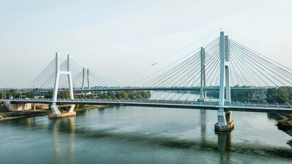 Obraz premium Modern cable-stayed bridge crossing over a calm wide river showcasing contemporary engineering design and urban infrastructure connectivity at sunset