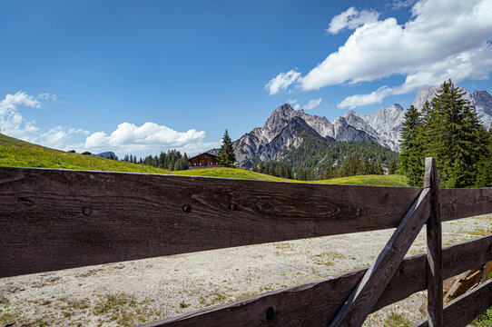 Nahaufnahme eines h&ouml;lzernen Koppelzauns auf der Litzlalm mit Blick auf Almh&uuml;tte und Bergmassiv.