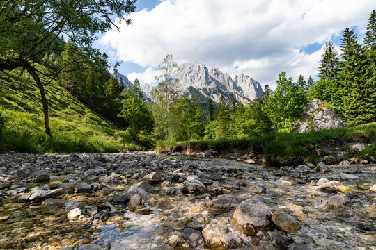 Glasklarer Bergbach mit Kieselsteinen im Vordergrund und Blick auf die Loferer Steinberge.