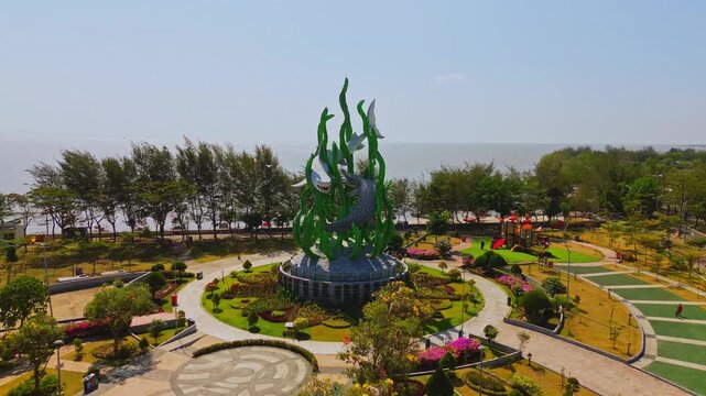 Aerial view of the giant Suroboyo statue featuring a shark and crocodile surrounded by a landscaped park, trees, and the coastline in Surabaya, East Java, Indonesia.