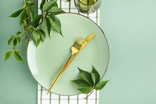 Elegant Thanksgiving Table Setting with Golden Cutlery and Fresh Green Leaves on Pastel Background