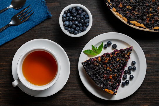 Slice of homemade blueberry pie with cup of tea. Top-down view of delicious blueberry pie slice served with cup of hot tea and fresh berries on dark wooden table
