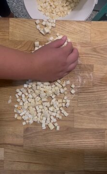 Top-down footage of a cook using a sharp stainless steel knife to finely slice and dice celeriac root on a wooden cutting board.