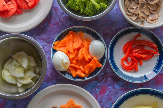 Fresh vegetables and eggs arranged for a healthy meal. Vibrant carrots, tomatoes, broccoli, and peppers. Eggs sit beside sliced onions and mushrooms. Plates hold colorful ingredients, ready to cook