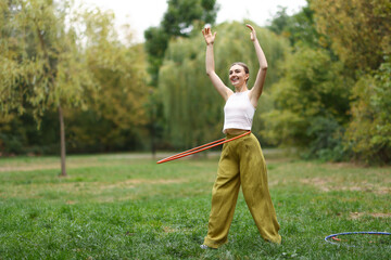 Athletic young woman exercising with hula hoop in park, space for text © New Africa
