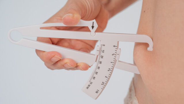 A woman measures the amount of subcutaneous fat on her abdomen using a caliper.