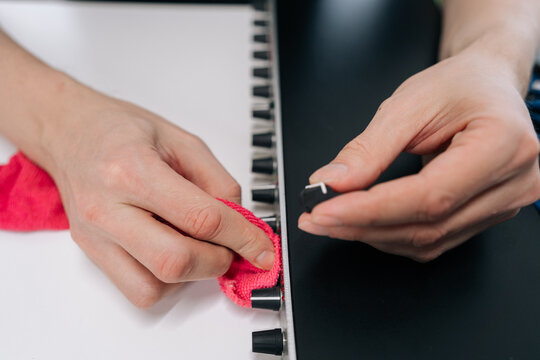 Musician hands cleaning and maintaining synthesizer, wiping white surface with cloth while removing knob, showing maintenance of studio audio gear.