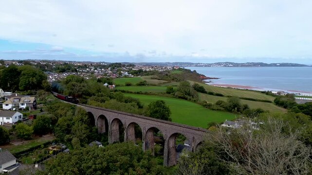 Old Steam Railway Train Crossing Viaduct in Paignton, with Broadsands Beach in the background, South Devon, England - 4K Drone Video