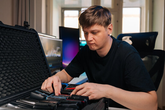 Young man diligently organizing multiple storage devices inside specialized protective case, preparing for data transfer or video editing project at professional workstation.