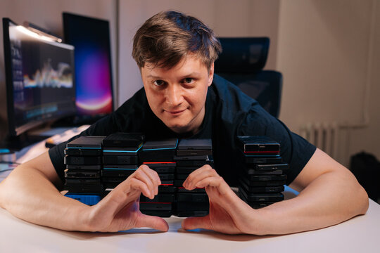 Man shows passion for data storage, making heart sign over many stacked external hard drives. Concept for digital backup, information management, love for technology in modern creative workspace.
