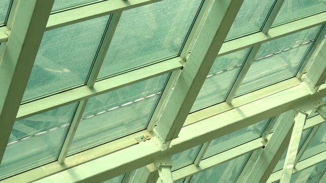 Modern architectural glass roof structure features geometric steel frames on bright sunny day. Contemporary skylight canopy offers clean geometric lines with daylight illuminating interior.