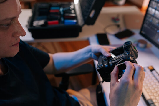 Photographer at workstation inserting memory card into professional digital camera, preparing for shoot or transferring data for post production editing.