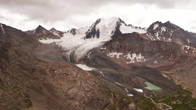 Aerial view of the glacial Ala-Kul Lake surrounded by rugged mountain peaks, rocky slopes, and snowfields in Ak-Su, Issyk-Kul Region, Kyrgyzstan.