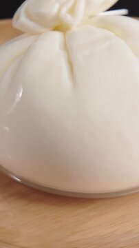 Vertical close up shot of fresh Italian burrata cheese ball rotating slowly on wooden plate.