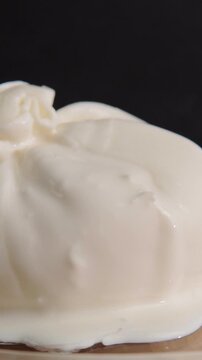 Vertical close up shot of cutting burrata cheese pouch with fork and knife releasing creamy filling.