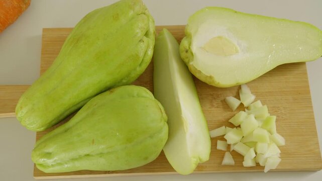 Top view of whole chopped and sliced chayote squash on a wooden cutting board
